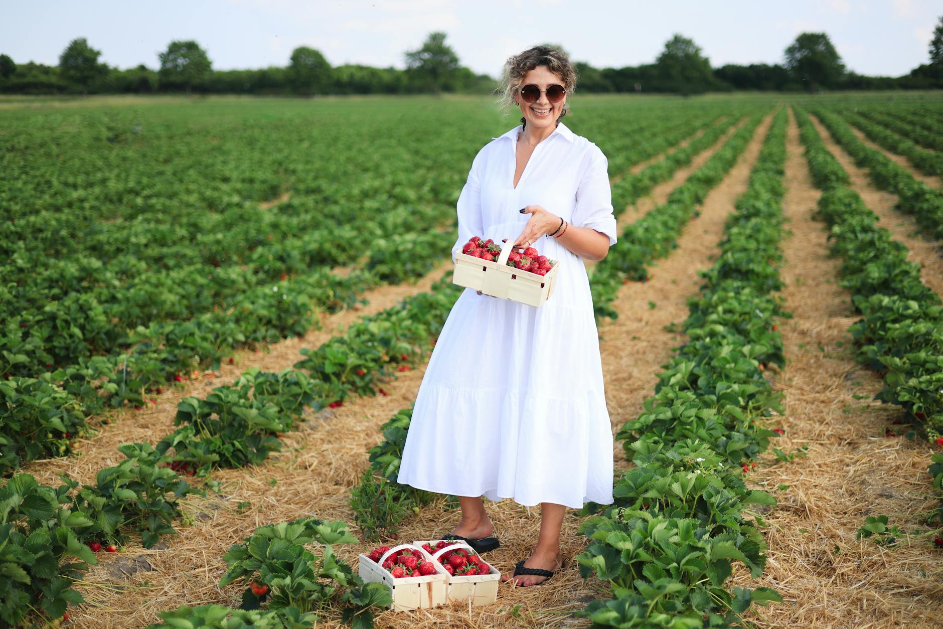smiling woman in sunglasses standing in white dress on rural field